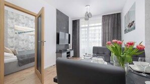 Uma sala de estar moderna com sofá, mesa de jantar com cadeiras, televisão na parede e janela com cortinas.