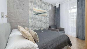 Quarto moderno com uma cama grande, uma parede cinzenta com design geométrico, um quadro e vista para um edifício através de cortinas leves.