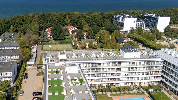 Um hotel com vários andares, piscina no terraço, cercado por vegetação e vista para o mar.