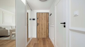 Een gang met een houten deur, witte muren en een lichtgekleurde vloer.