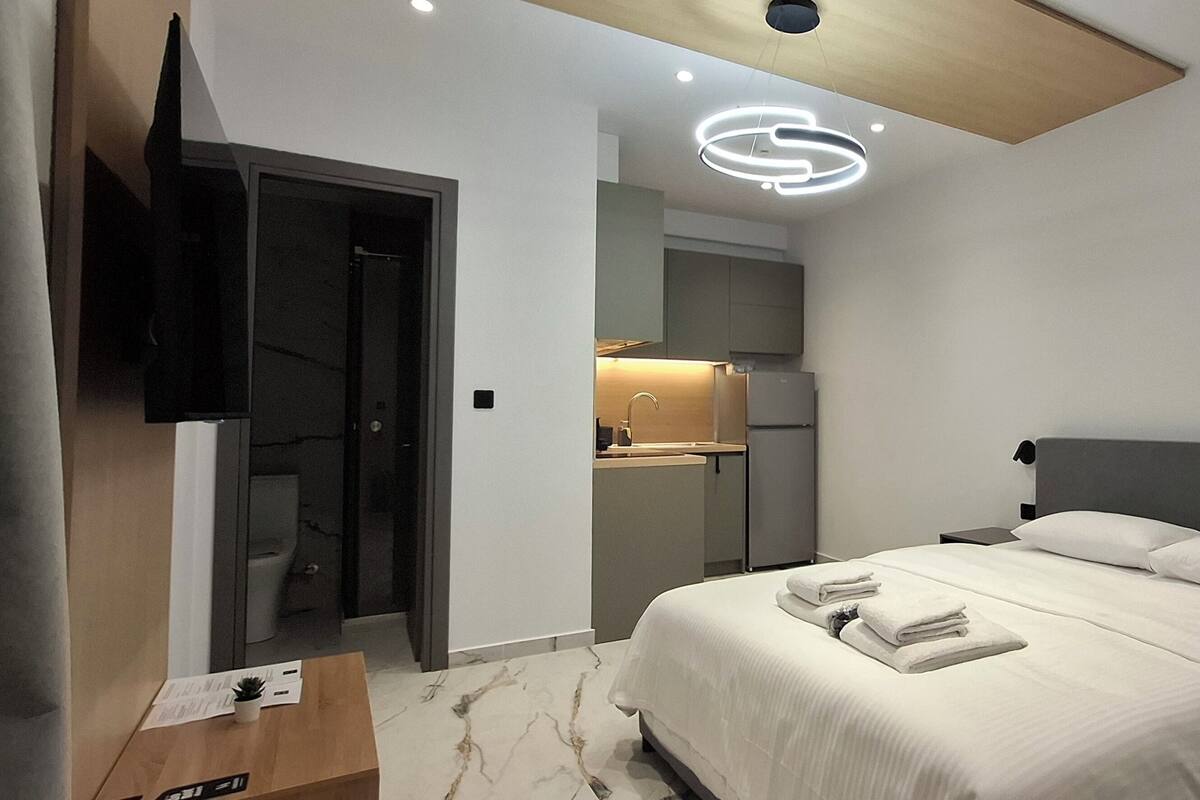 A modern bedroom with a large bed, a TV mounted on the wall, and a ceiling light fixture.