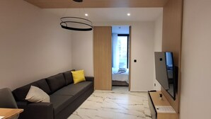 A modern living room with a dark sofa, a flat-screen TV, and a marble floor. - Ilion Apartments (Thessaloniki)