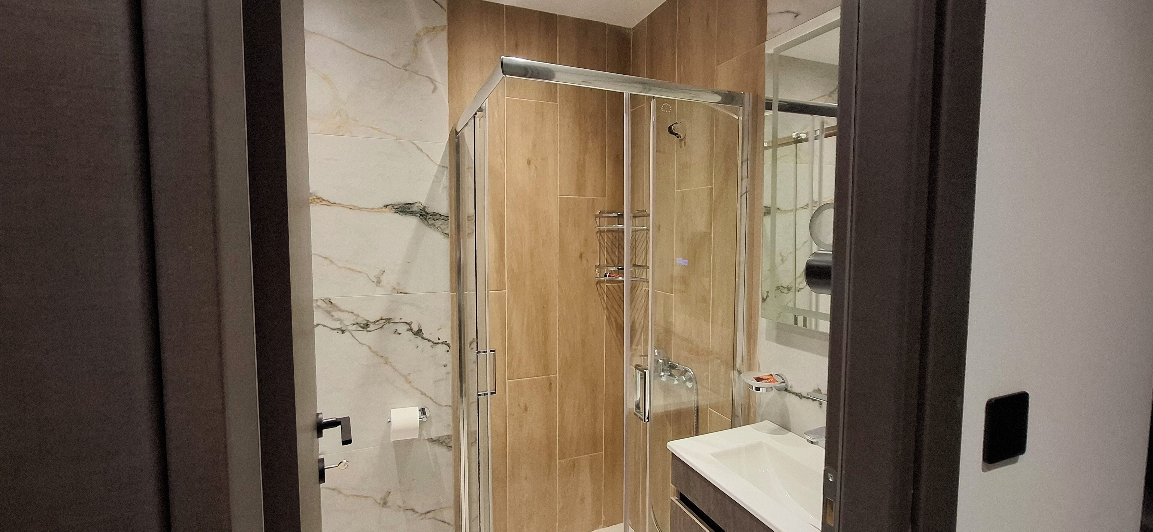 A modern bathroom with a glass-enclosed shower, marble walls, and a wooden vanity.