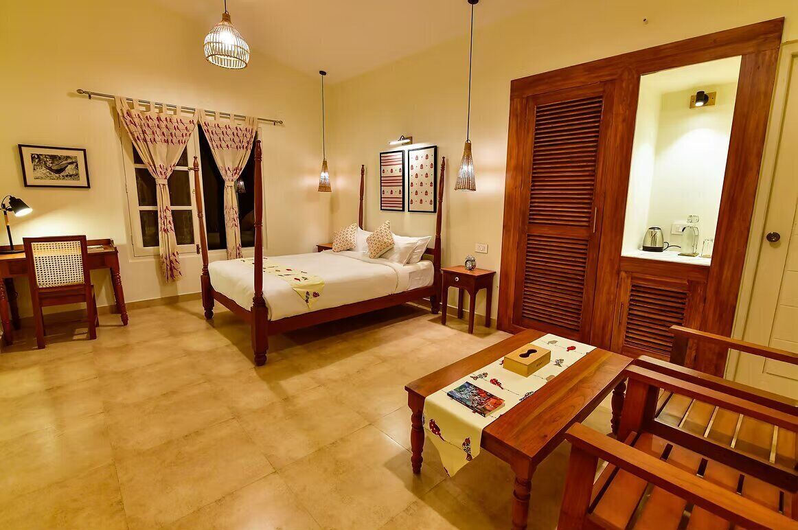 A four-poster bed with a wooden frame, a bedside table with a magazine, a chair, and a dining table with a placemat.