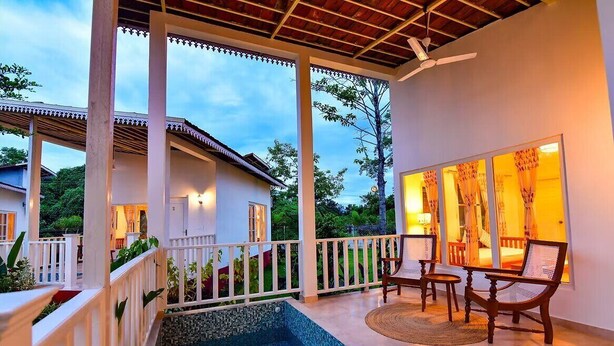 A covered outdoor area with a pool, wooden furniture, and a view of a house in the background. - Musafir Jungle Resort (Sarupeta)