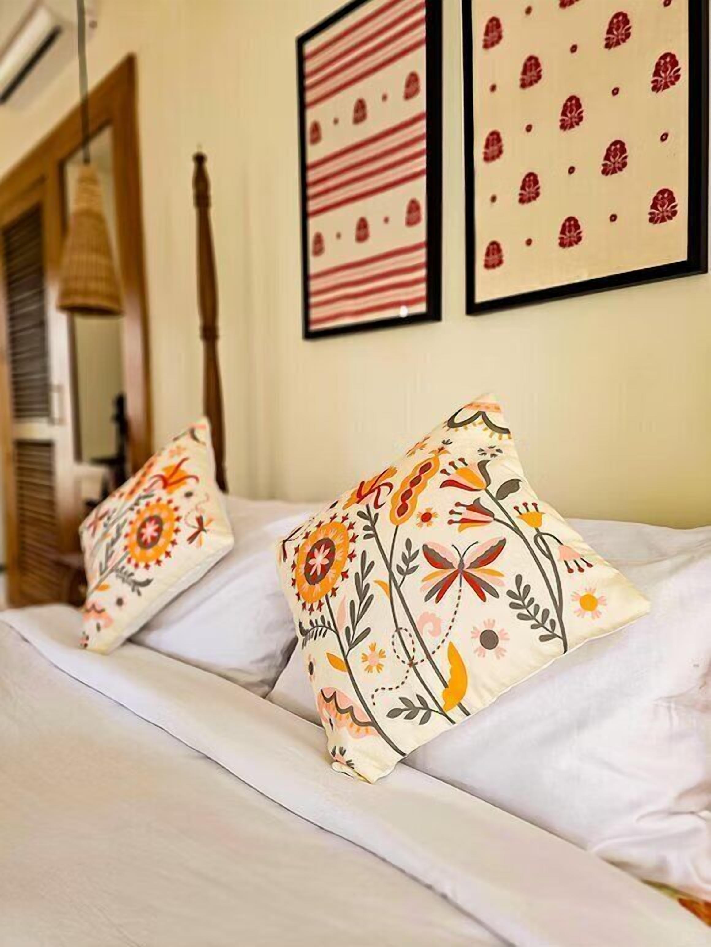 Een hotelkamer met een bed, twee sierkussens, een hanglamp en twee kunstwerken in lijsten aan de muur.