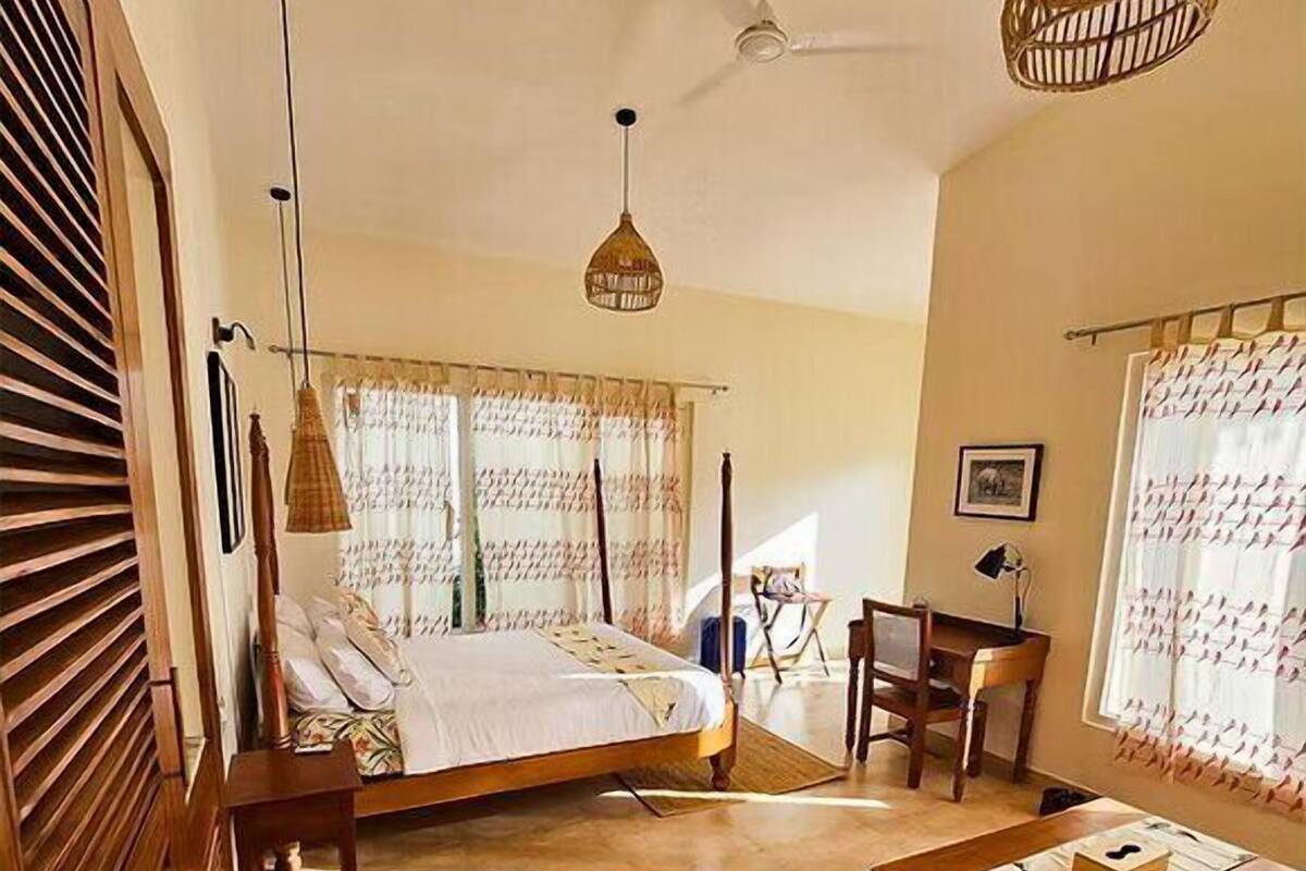 A bedroom with a bed, a desk, and a chair, a ceiling fan, and a hanging light fixture.