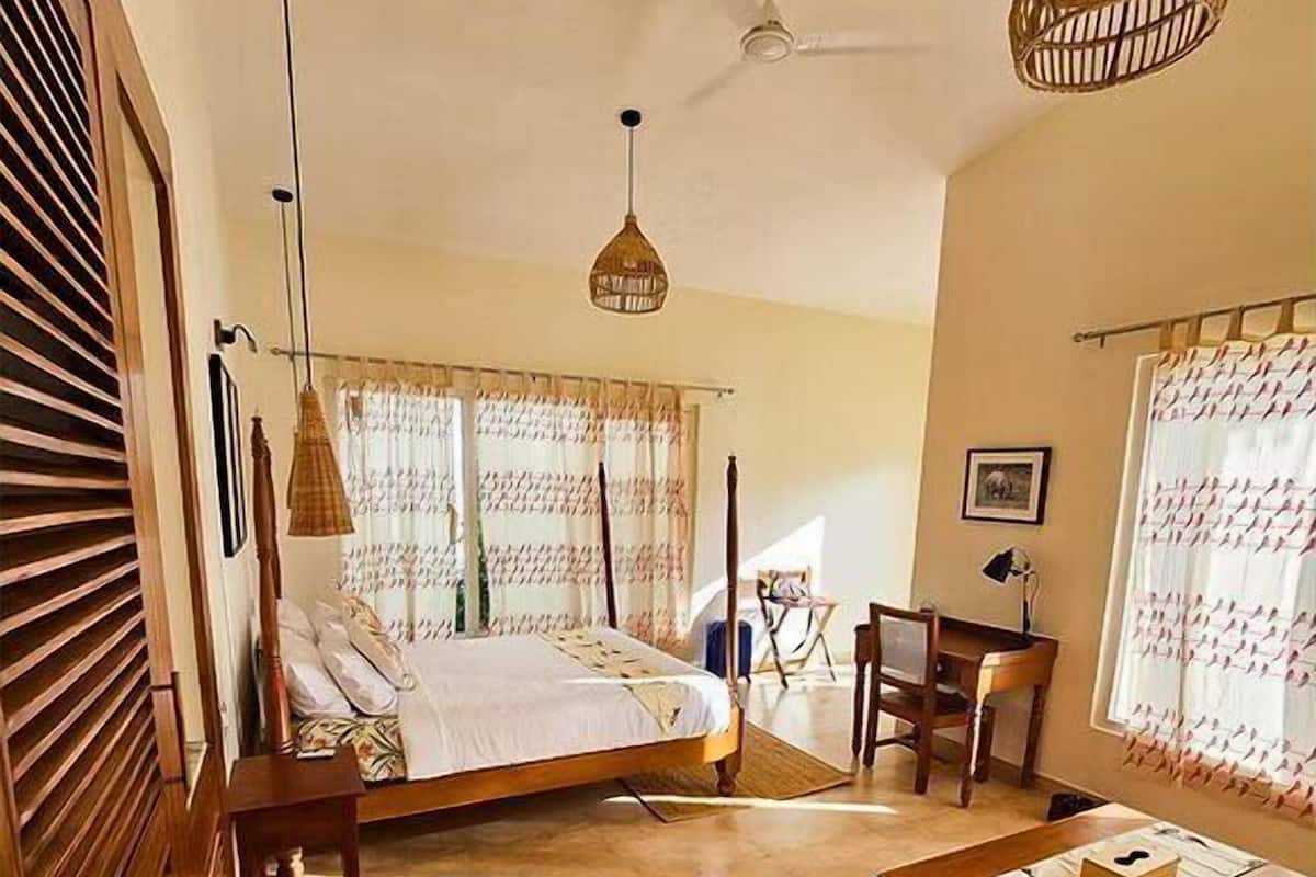 A bedroom with a bed, a desk, and a chair, a ceiling fan, and a hanging light fixture.