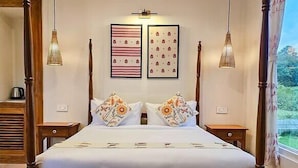 A four-poster bed with a wooden frame, white bedding, and floral pillows. There are two wall-mounted picture frames above the bed, and two pendant lights hanging from the ceiling. - Musafir Jungle Resort (Sarupeta)