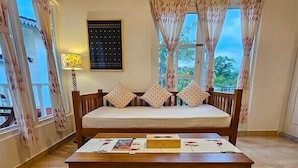 A bedroom with a bed, a wooden nightstand, a bedside table, and a window with curtains. - Musafir Jungle Resort (Sarupeta)