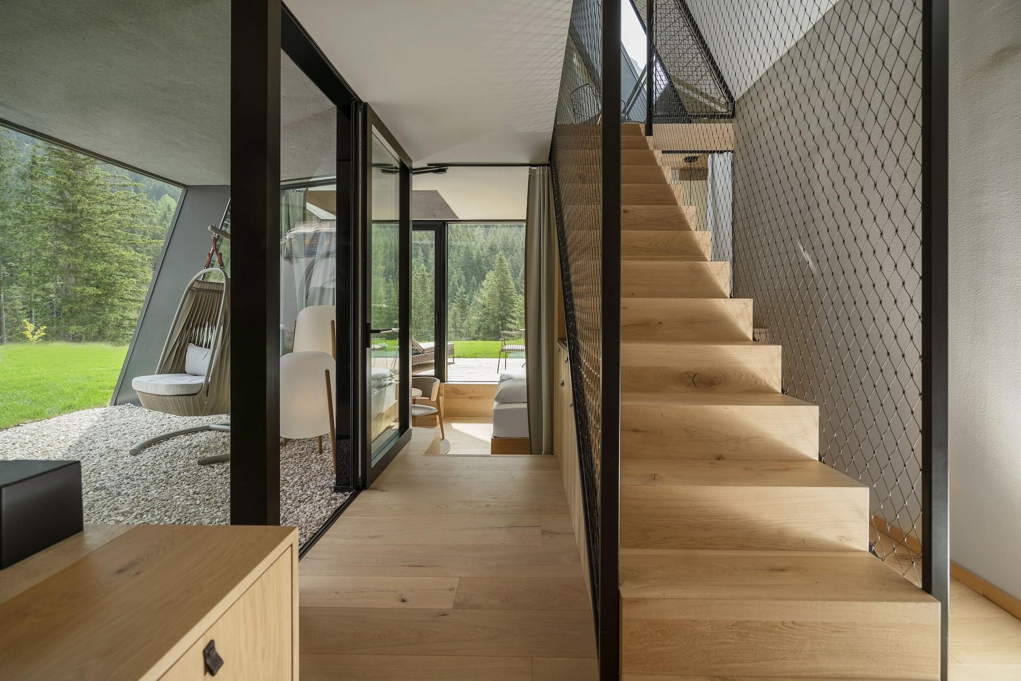 A modern interior with a wooden staircase, glass doors leading to a balcony, and a view of a green landscape.