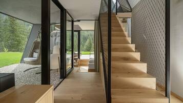 A modern interior with a wooden staircase, glass doors leading to a balcony, and a view of a green landscape.