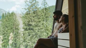 A couple sitting on a wooden bench by a window overlooking a forested area.