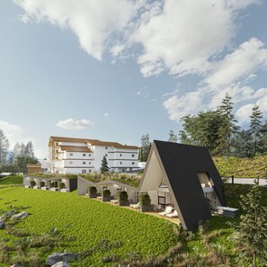 A modern building with a flat roof and a sloped roof section, surrounded by green fields and trees. - Olympic Spa Hotel (San Giovanni di Fassa)
