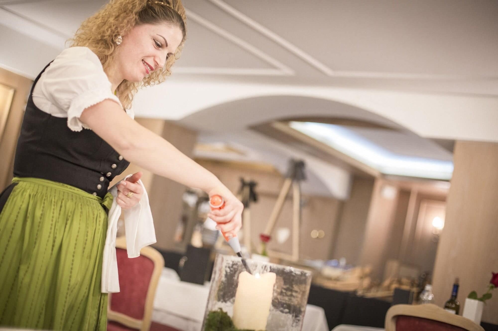 Eine Person in traditioneller Kleidung bereitet eine Kerze in einem Raum mit einem Chandelier und einem Tisch mit einer Flasche und einer Rose.
