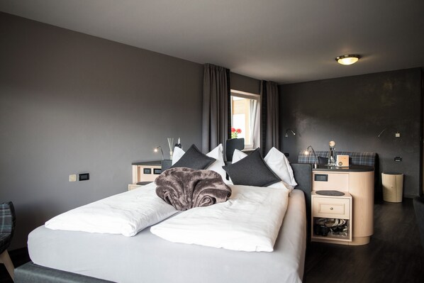 A modern hotel room with a large bed, two bedside tables, a nightstand, and a window with curtains. - Olympic Spa Hotel (San Giovanni di Fassa)