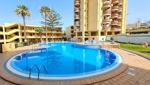 A swimming pool surrounded by yellow buildings with balconies, palm trees, and a lifebuoy. - Vacation Apartment 'Sunshine Sea' with Sea View, Wi-Fi, and Air Conditioning (Arona)