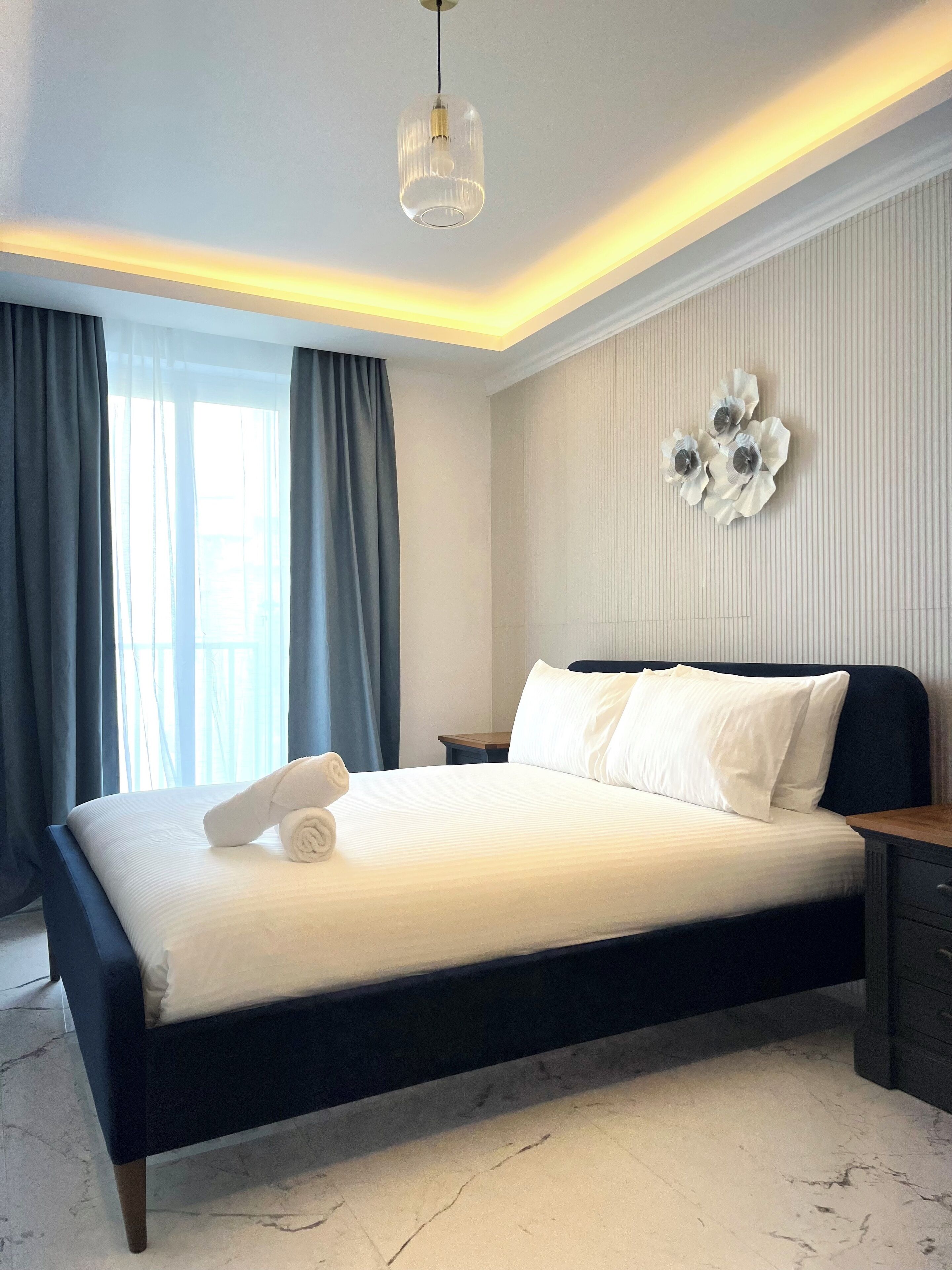 A modern bedroom with a bed, a nightstand, a wall-mounted flower decoration, and a ceiling light fixture.