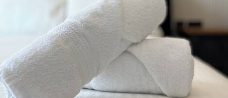 A neatly made bed with white linens and a folded towel on top.