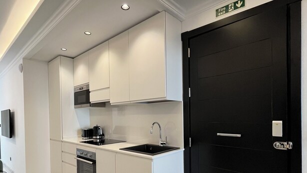 Una cocina moderna con armarios blancos, una puerta negra y suelo de mármol.