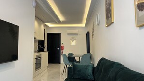 Una sala moderna con un sofá verde oscuro, un televisor de pantalla plana montado en la pared y un comedor con mesa y sillas.