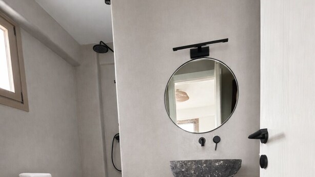 Une salle de bain moderne avec un miroir rond, un lavabo en forme de coupe et des paniers en osier placés sur des étagères.