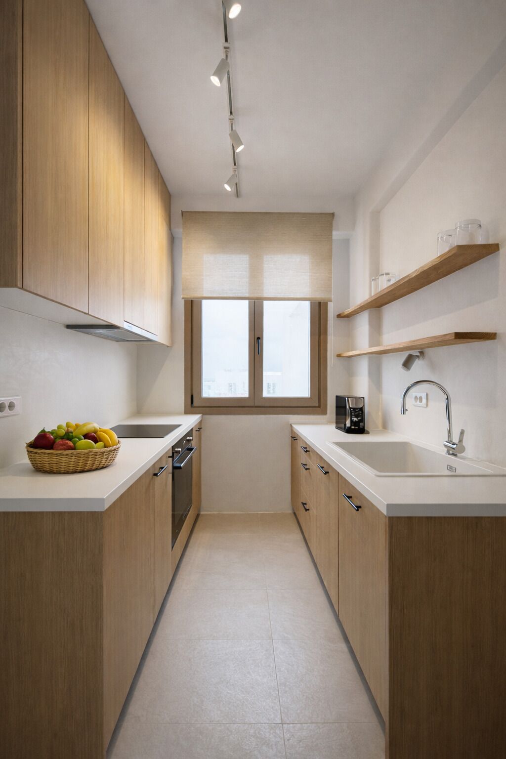 Een smalle keuken met houten kastjes, een raam en een aanrecht met een mand vol fruit.