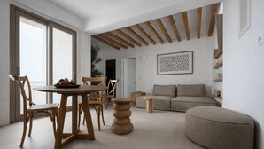 Un salon moderne avec une table ronde en bois, deux chaises en bois, un canapé beige et un pouf rond.