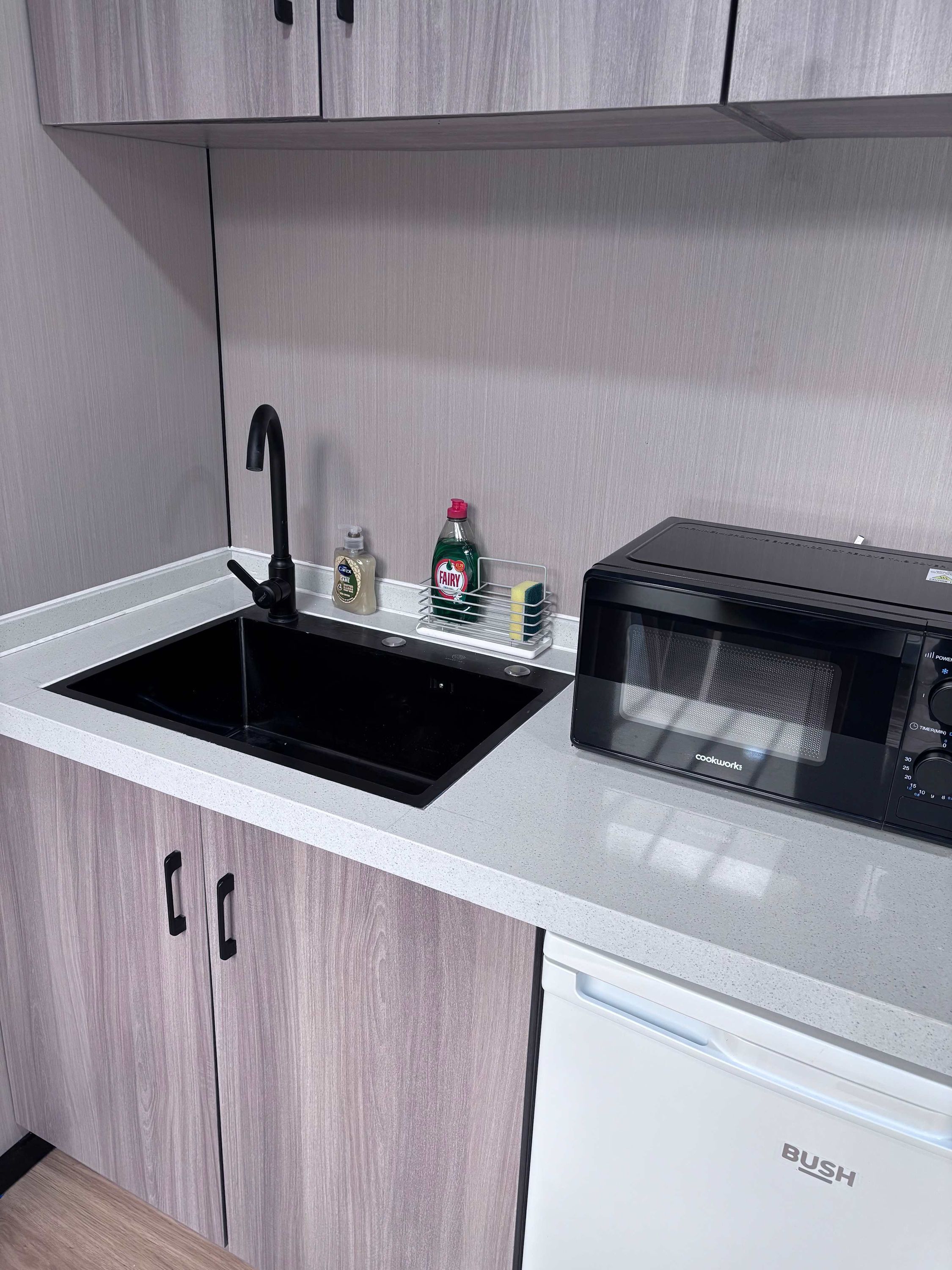 A kitchen with a black sink, a microwave, and a dish rack.