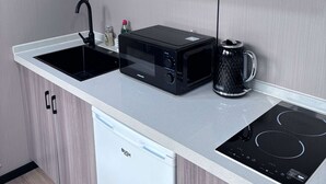 Eine moderne Küche mit grauen Schränken, einer weißen Arbeitsplatte, einer schwarzen Mikrowelle, einer Kaffeemaschine und einem Geschirrspüler.