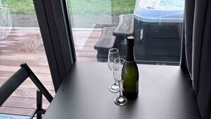 Ein Tisch mit einer Flasche und zwei Gläsern, ein Stuhl sowie ein Blick auf ein Whirlpool und einen Garten.