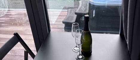 Una mesa con una botella y dos vasos, una silla, y una vista de un jacuzzi y un jardín al exterior.