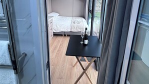 Ein modernes Zimmer mit einem Bett, einem kleinen Tisch mit Flasche und Glas sowie einem Fernseher an der Wand.