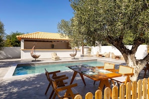 A poolside area with a dining table, chairs, and a covered seating area. - Eneos Boutique Residence - Koroni Garden Gem (Pylos-Nestoras)