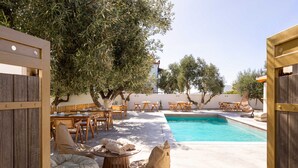 An outdoor pool area with wooden furniture, including chairs and a table, surrounded by olive trees. - Eneos Boutique Residence - Koroni Garden Gem (Pylos-Nestoras)