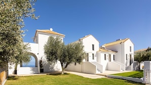 A white building with a tiled roof, a well-maintained lawn, and a clear blue sky. - Eneos Boutique Residence - Koroni Garden Gem (Pylos-Nestoras)