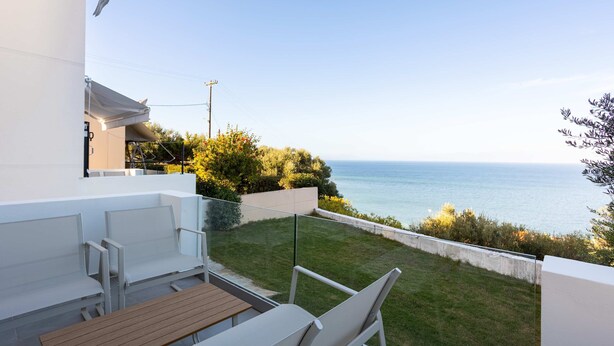 A balcony with a view of the sea, white outdoor furniture, and a wooden table. - Eneos Boutique Residence - Koroni Garden Gem (Pylos-Nestoras)