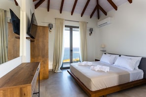 A bedroom with a bed, a desk, a TV, and a view of the sea. - Eneos Boutique Residence - Koroni Garden Nest (Pylos-Nestoras)