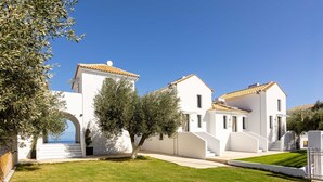 A white building with a tiled roof, a well-maintained lawn, and a clear blue sky. - Eneos Boutique Residence - Koroni Garden Nest (Pylos-Nestoras)
