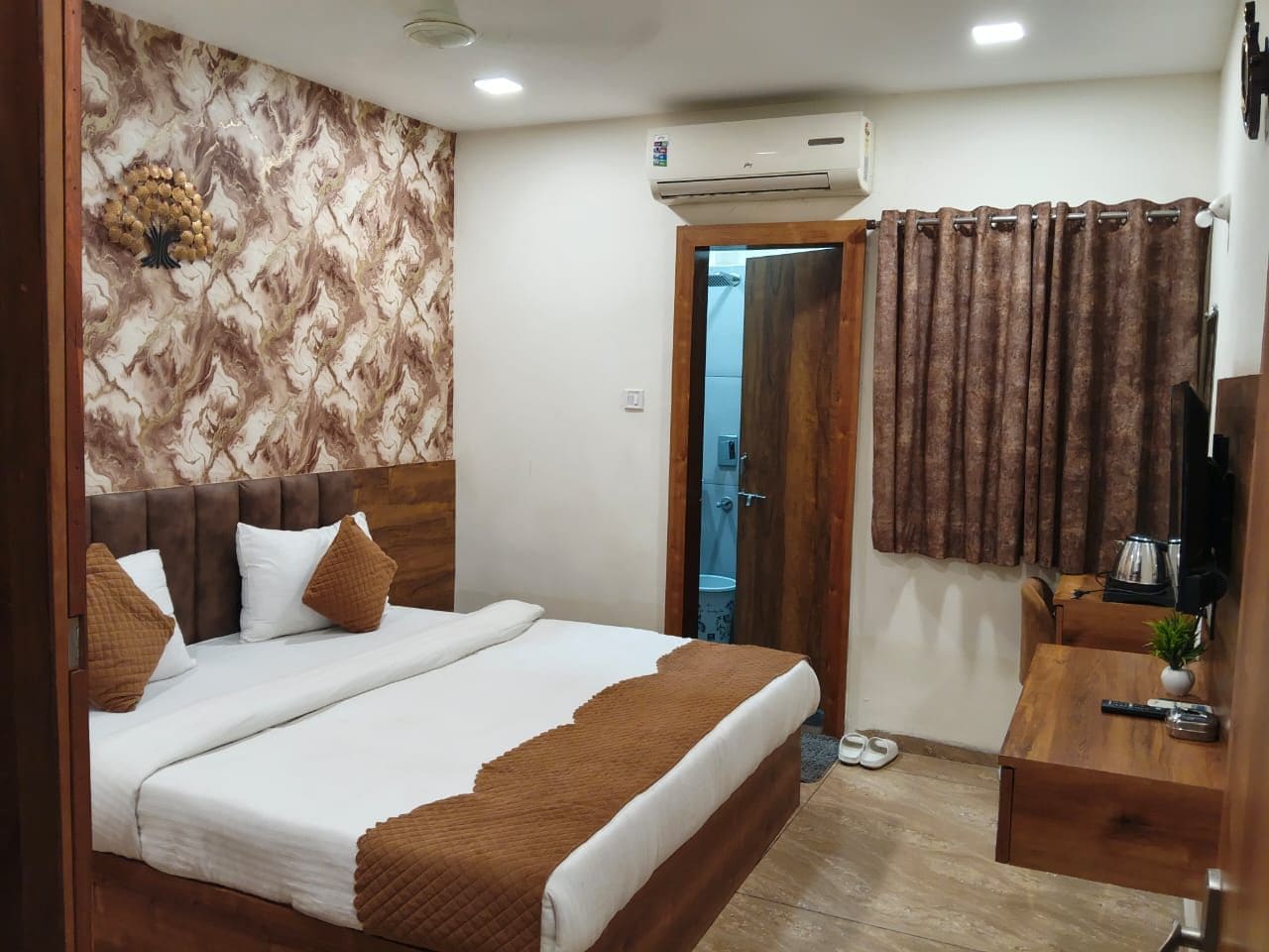 Une chambre d’hôtel équipée d’un lit, d’un bureau, d’un appareil de climatisation, d’une télévision et d’une salle de bain visible à travers une porte ouverte.