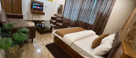 A modern bedroom with a bed, a TV, a desk, and a sofa.