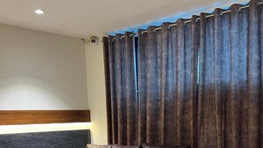 A modern living room with a brown leather sectional sofa, a glass coffee table, and a dark wall with a wooden accent strip. - Hotel Central Point (Indore)