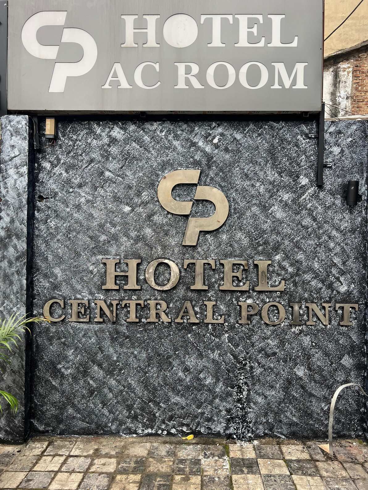 L’entrée d’un hôtel, avec une enseigne indiquant « CHAMBRES CLIMATISÉES » et « HÔTEL, EMPLACEMENT CENTRAL ».