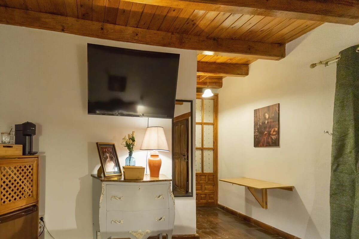 Une pièce chaleureuse avec un plafond en bois, une commode blanche à tiroirs, une petite table avec une lampe et un tableau accroché au mur.