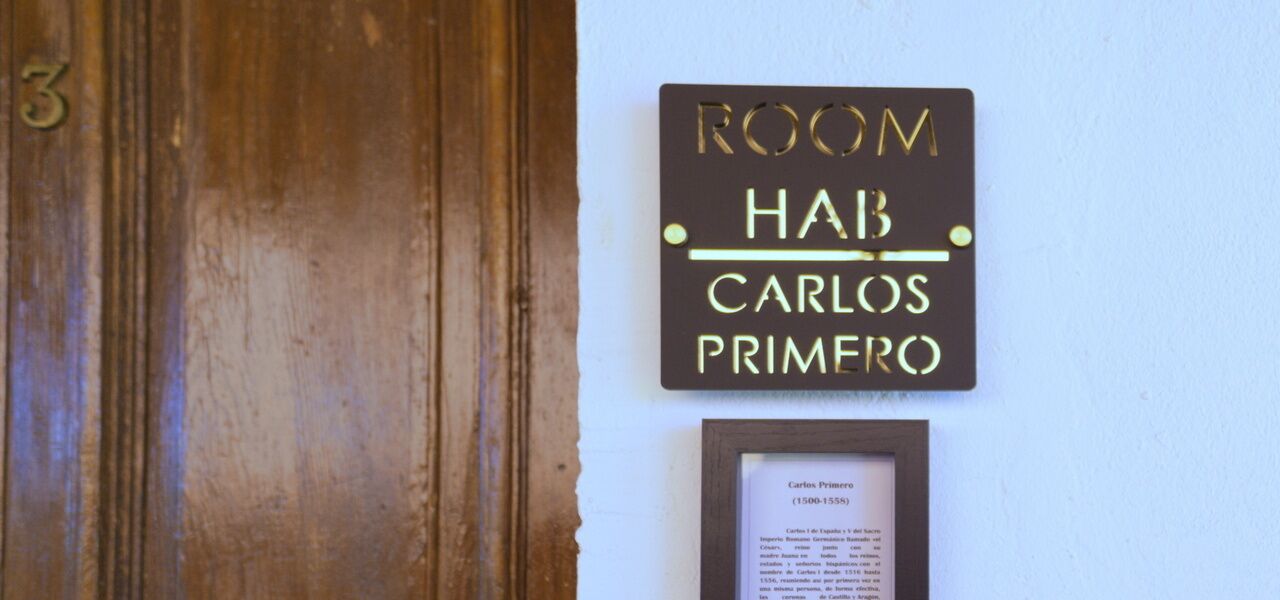 Eine Holztür mit einem Schild darüber, auf dem 'ROOM HAB CARLOS PRIMERO' steht.
