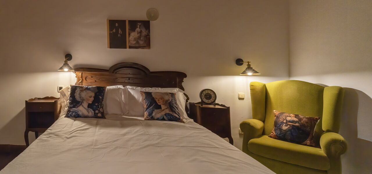 Ein Schlafzimmer mit einem großen Bett, einem grünen Sessel, zwei Nachttischen und Wandleuchten.