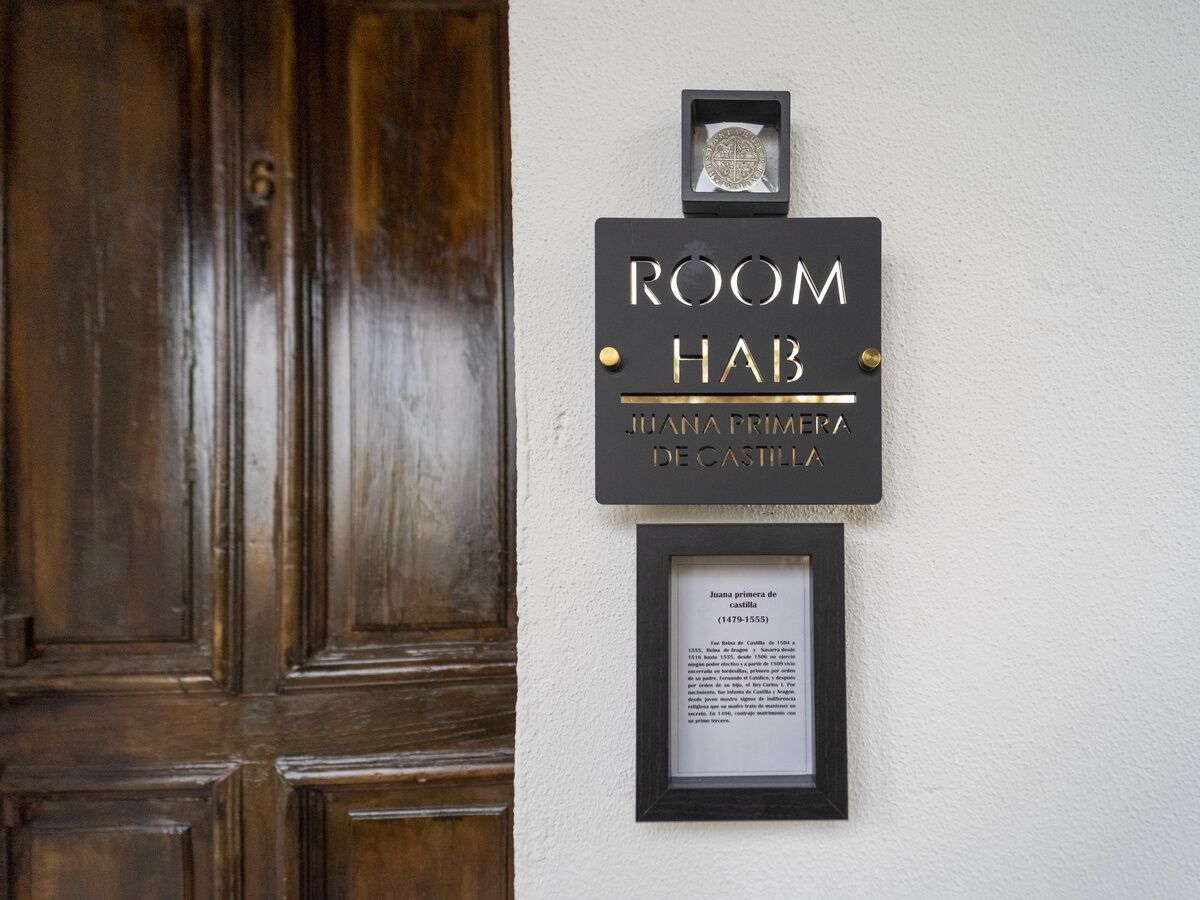 A sign for 'ROOM HAB JUANA PRIMERA DE CASTILLA' with a plaque below it.