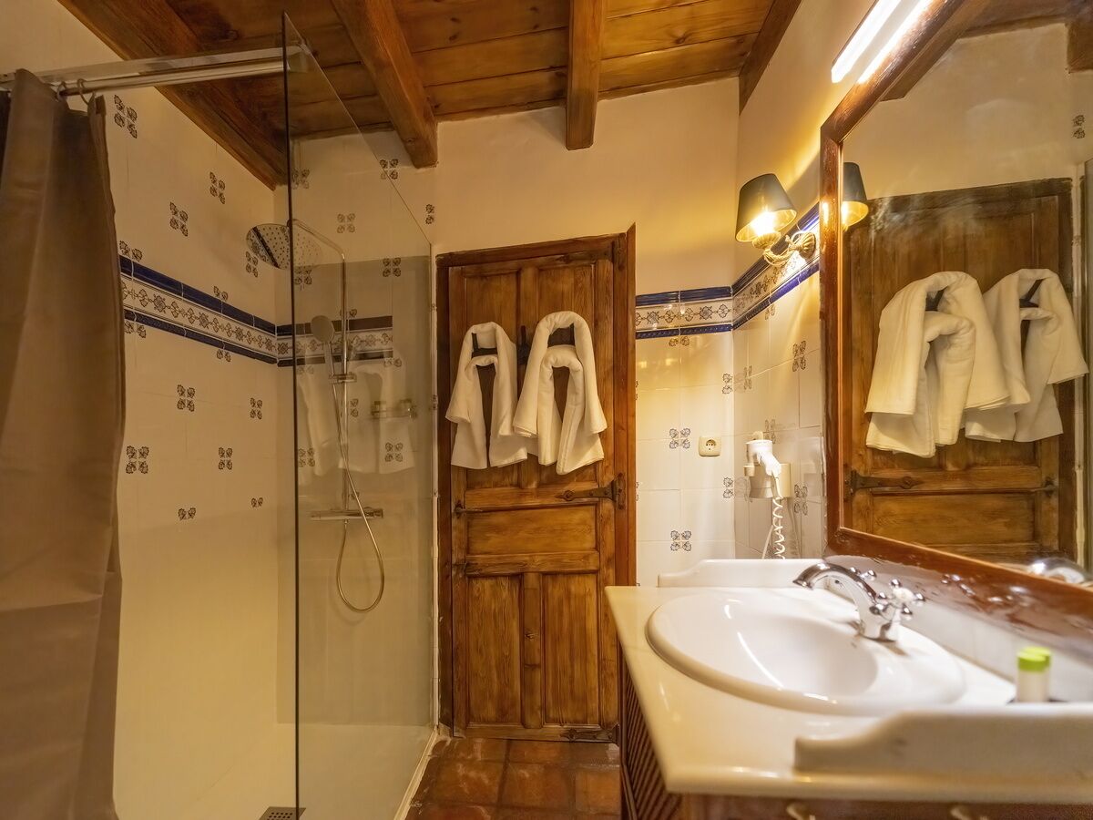 Un bany amb una porta de fusta, un box de dutxa de vidre i un lavabo amb mirall.