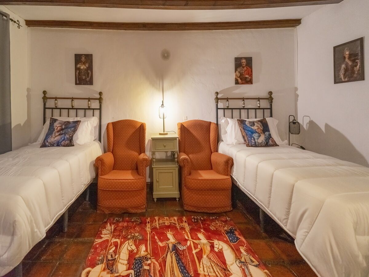 Una habitación con dos camas individuales, una mesita pequeña, dos sillas y una alfombra estampada.