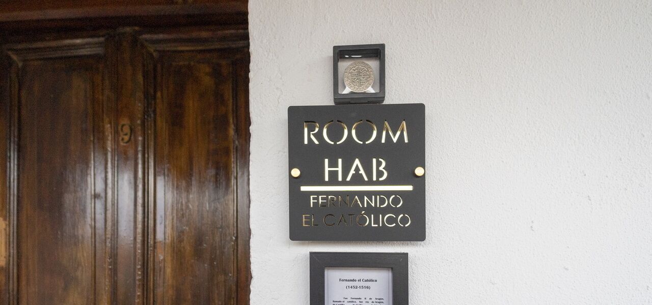 A sign for "ROOM HAB" with the name "FERNANDO EL CATOLICO" and a framed certificate below it.